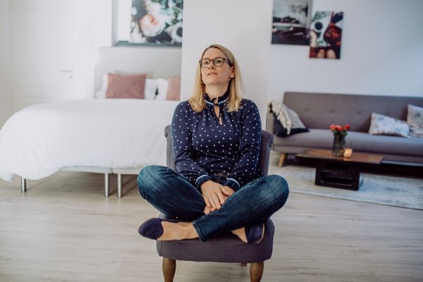 Katrin Weber sitzt nachdenklich auf einem Stuhl. Ihr Blick geht Richtung Decke.